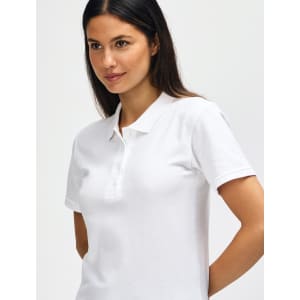 A woman wearing a white Gildan Softstyle Ladies' Double Pique Polo with a collar and buttons, featuring a logo.