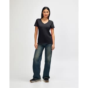A model wearing a black Gildan Softstyle ladies' V-neck t-shirt paired with blue jeans and white shoes.