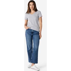 A woman stands wearing a grey Gildan Softstyle ladies' v-neck t-shirt and blue jeans, paired with white sneakers.