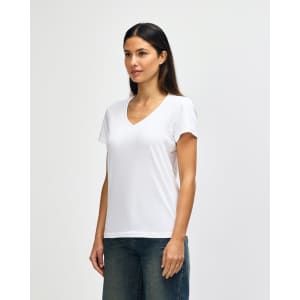 A white Gildan Softstyle ladies' V-neck T-shirt displayed on a model, paired with blue jeans. Features a logo.