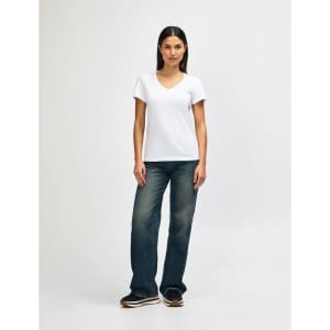 A model wearing a white Gildan Softstyle Ladies' V-Neck T-Shirt paired with blue jeans and white sneakers.