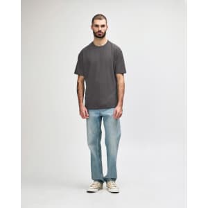 A midweight adult t-shirt in olive green, paired with black jeans and sneakers. The model is walking.