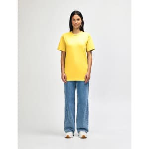 A midweight adult t-shirt in bright yellow, paired with black pants and black sneakers, featuring a logo.