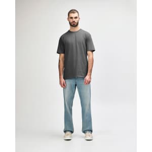 A grey Gildan Softstyle midweight T-shirt displayed on a model, paired with light blue jeans and casual shoes.