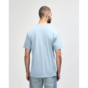 A person wearing a blue Gildan Softstyle adult midweight T-shirt, viewed from the back. The shirt has a logo.