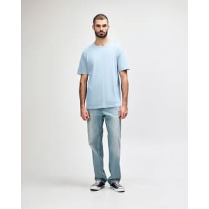 A midweight adult T-shirt in light blue, worn by a model with dark pants and sneakers, featuring a logo.