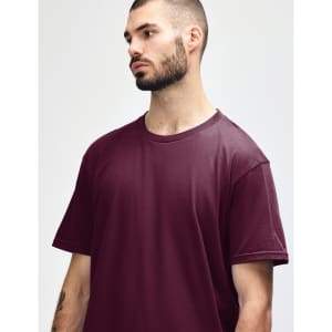 A man wearing a burgundy Gildan Softstyle adult midweight t-shirt, featuring a simple design and short sleeves.