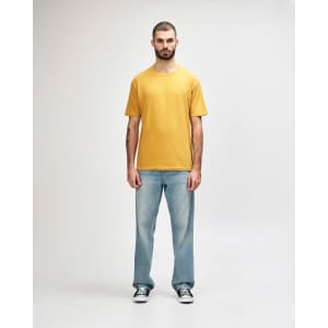 A man wearing a mustard yellow Gildan Softstyle adult midweight t-shirt and black jeans, walking casually.
