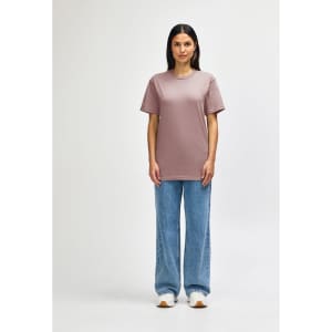 A midweight adult T-shirt in soft pink, worn with black jeans and sneakers. Features a logo.