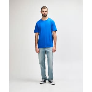 A man wearing a blue Gildan Softstyle adult midweight T-shirt paired with light denim jeans and white shoes.