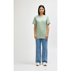 An olive green midweight t-shirt worn by a model, paired with black jeans and sneakers, featuring a logo.