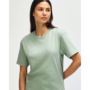 A model wearing a midweight T-shirt in a soft green colour. The T-shirt has a simple design and features a logo.