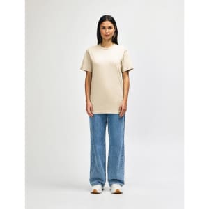 A light khaki midweight t-shirt is worn by a model paired with black pants and sneakers, also featuring a logo.