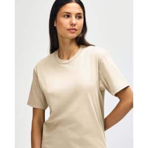 A midweight adult T-shirt in a neutral beige colour, displayed on a model with a casual pose. The shirt features a logo.