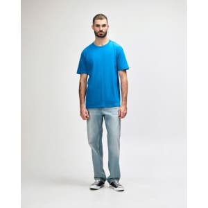 A man wearing a bright blue Gildan Softstyle adult midweight T-shirt and black jeans, with a casual stance.