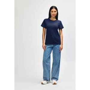 A woman wearing a navy Gildan Softstyle ladies midweight T-shirt, paired with blue jeans and white sneakers.