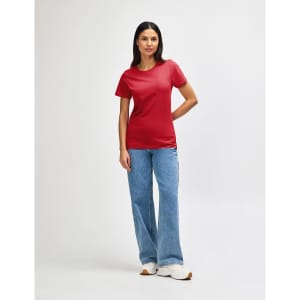 A red Gildan Softstyle ladies midweight T-shirt displayed on a model, paired with blue jeans and white shoes.
