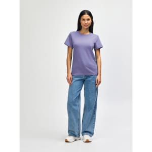 A purple midweight t-shirt is worn with blue jeans and white shoes, featuring a logo on the shirt.
