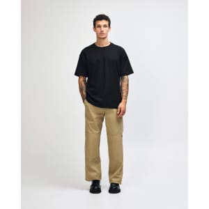 A model wears a black American Apparel Super Heavyweight T-Shirt paired with olive-green trousers and white sneakers.