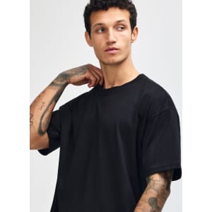A model wearing a black American Apparel Super Heavyweight T-Shirt, featuring a relaxed fit and visible tattoos.