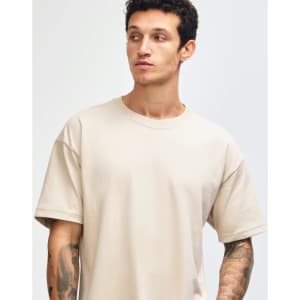 A light beige super heavyweight T-shirt on a model, featuring a relaxed fit and short sleeves. It has a logo.