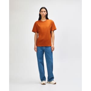 A model wearing an orange heavyweight t-shirt paired with olive green cargo pants and white sneakers, standing against a plain background.