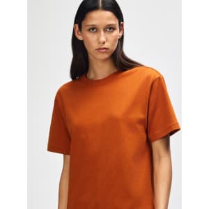 An orange American Apparel Super Heavyweight T-Shirt on a model, featuring a round neckline and short sleeves.