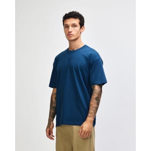 A model wearing a dark teal oversized T-shirt with short sleeves. The shirt has a simple design and a logo.