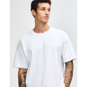 A model wearing a plain white American Apparel Super Heavyweight T-Shirt. The shirt has a casual fit and features a logo.