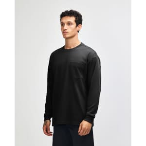 A black long-sleeve t-shirt featuring a pocket, modelled by a person with curly hair. The shirt has a logo.