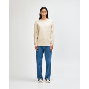 A model wearing a beige long-sleeve T-shirt with a pocket paired with olive green pants and casual sneakers.