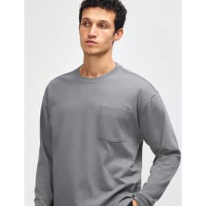 A model wearing a grey long-sleeve t-shirt with a pocket and a logo on the chest.