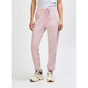 Unisex sweatpants in soft pink, featuring an elastic waistband and cuffs, shown with a pair of sneakers.