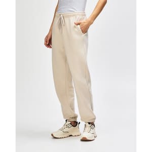 Unisex sweatpants in a light beige colour, featuring a logo, styled with a pink top and white sneakers.