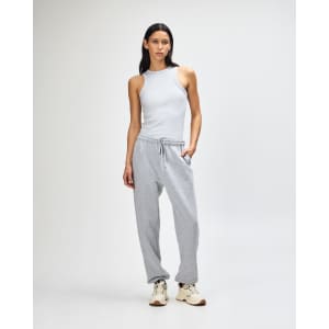 Unisex sweatpants in grey, featured with a cropped cream top, model standing in casual pose, includes branding.