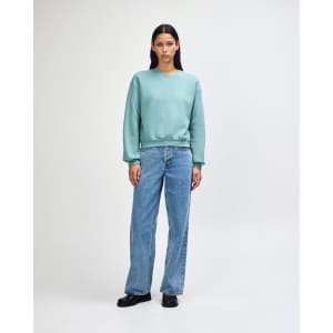A woman wearing a teal crewneck sweatshirt with a relaxed fit, paired with loose light blue jeans.