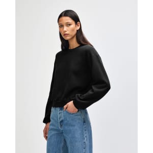 A women's black crewneck sweatshirt displayed on a model, featuring long sleeves and a relaxed fit.