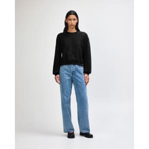 A black crewneck sweatshirt paired with light blue wide-leg jeans on a model. The sweatshirt has a logo.
