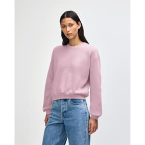 A woman wearing a pink American Apparel Reflex Fleece women's crewneck sweatshirt paired with blue jeans.