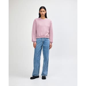 A light pink women's crewneck sweatshirt paired with blue wide-leg jeans and white sneakers. The sweatshirt has a logo.