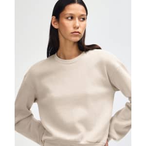 A cream women's crewneck sweatshirt with a casual fit, modelled by a woman. Featuring long sleeves and a simple design.