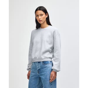 A grey women's crewneck sweatshirt with a relaxed fit and branding, styled with casual jeans.