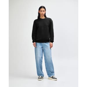 A unisex crewneck sweatshirt in black, paired with light blue cargo pants, featuring curly hair. The sweatshirt has a logo.
