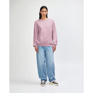 A unisex crewneck sweatshirt in light purple, paired with blue jeans and worn by a model. The sweatshirt has a branding logo.