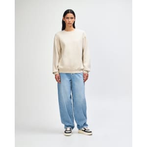 A unisex crewneck sweatshirt in beige worn with light blue jeans and black sneakers, featuring a logo.