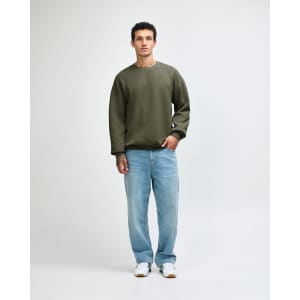 A unisex crewneck sweatshirt in olive green, paired with black cargo pants, worn by a model. Features a logo.