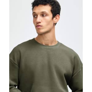 A man wearing an olive green unisex crewneck sweatshirt. The sweatshirt features a loose fit and has a logo.