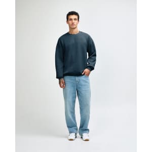 A unisex crewneck sweatshirt in a deep teal colour, paired with light blue cargo pants and styled on a model.