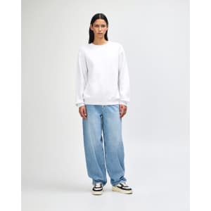 A unisex crewneck sweatshirt in white, paired with light blue baggy jeans, worn by a model. Features a branding logo.