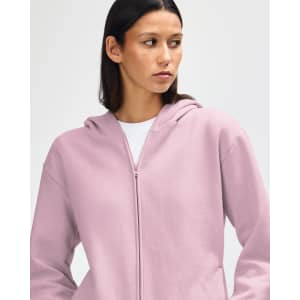 A unisex full zip hooded sweatshirt in a soft pink colour, featuring a hood and a brand logo.